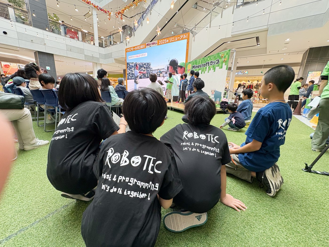 ロボテックのTシャツを着て、地区大会の発表を見守る生徒たちの後ろ姿