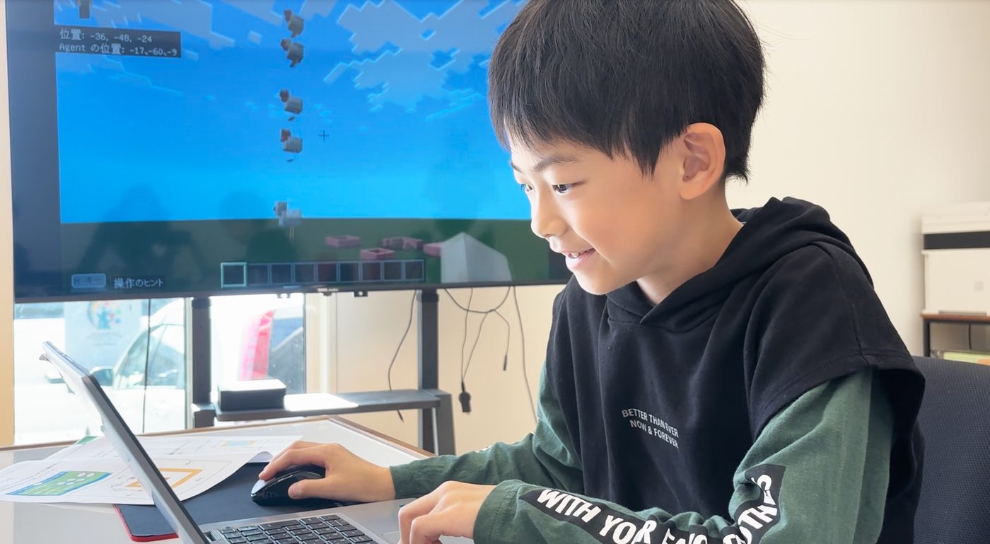 マインクラフト教育版の画面を見ながら、笑顔でパソコンを操作する生徒