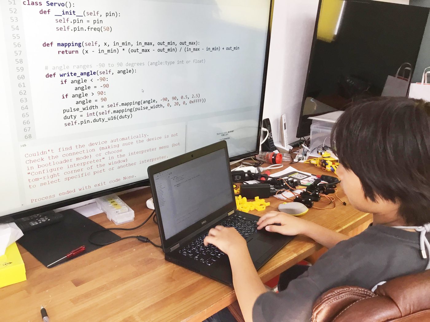 大画面に映したPythonのコードを見ながら、ノートパソコンでプログラムを書く生徒