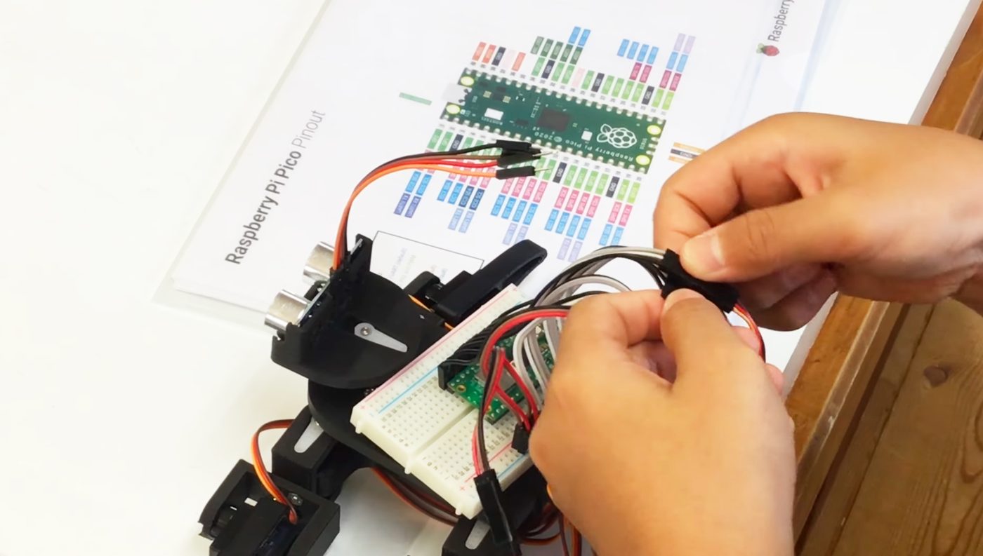 Raspberry Pi Pico のピン配置図を見ながら、自作ロボットの配線をする生徒の手元