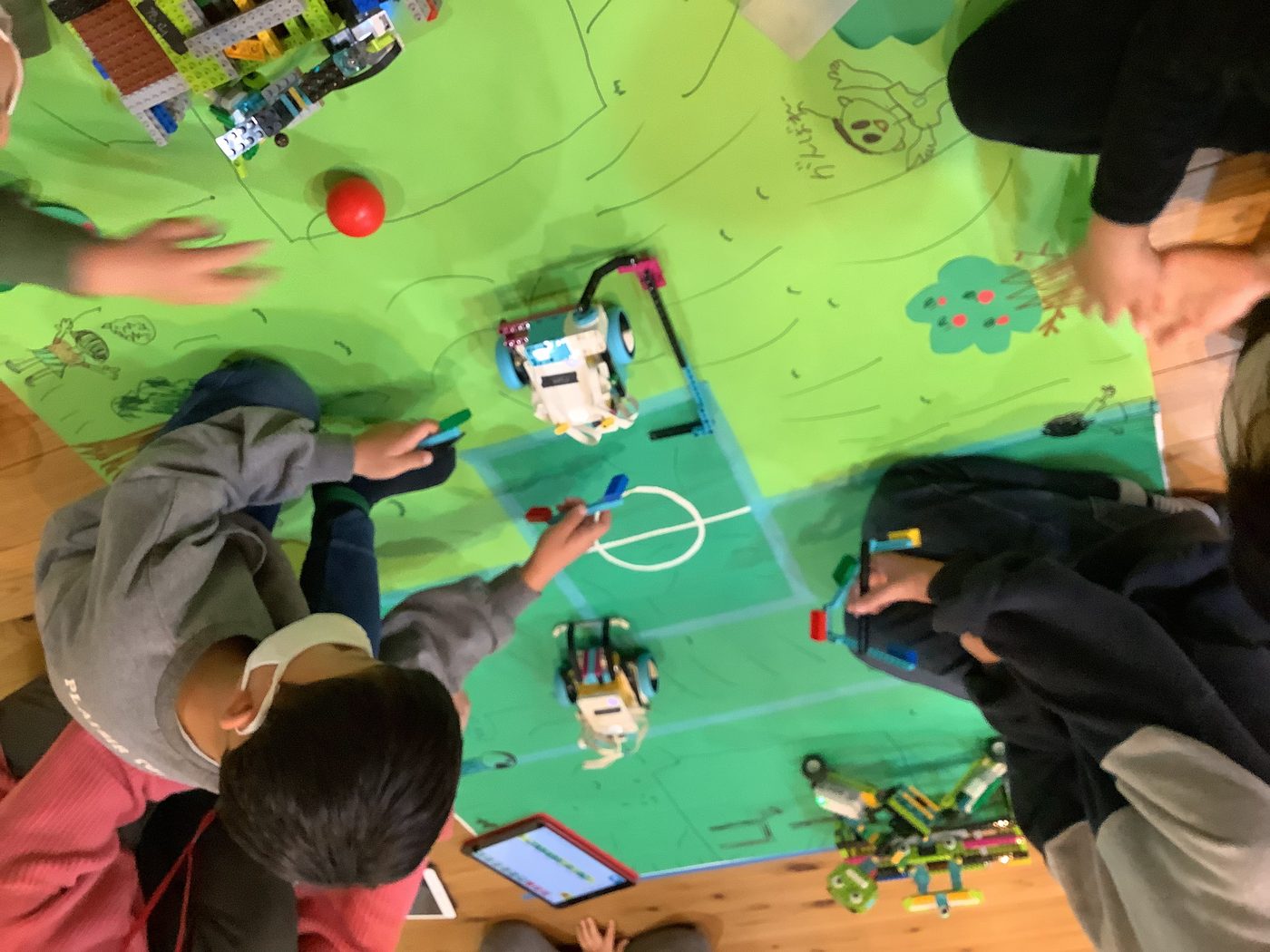 床に広げたコートを数人で囲み、自作ロボットで対戦する様子